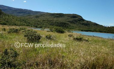 Landscape view of the land parcel featuring tall grasses, shrubs, and a lake surrounded by forested hills.